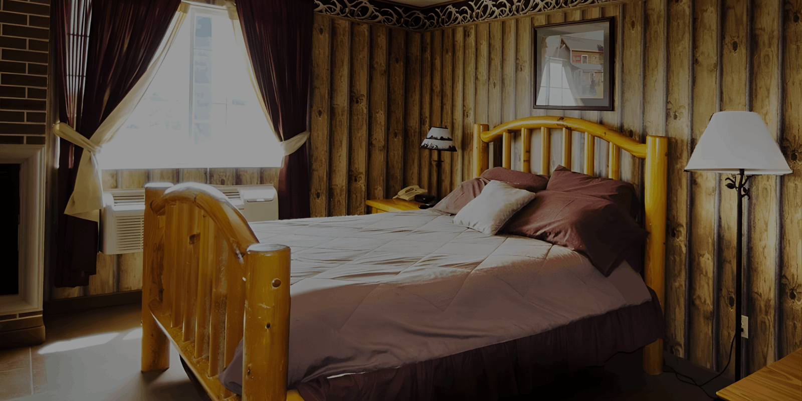 A rustic bedroom with a light-wood log bed frame, dark bedding, and vertical wood-paneled walls.