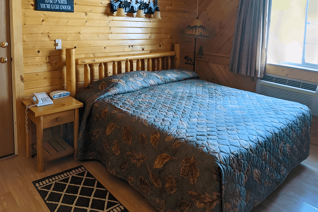 A rustic bedroom with log-style furniture, pine-paneled walls, and a bed covered in a blue and brown patterned comforter.