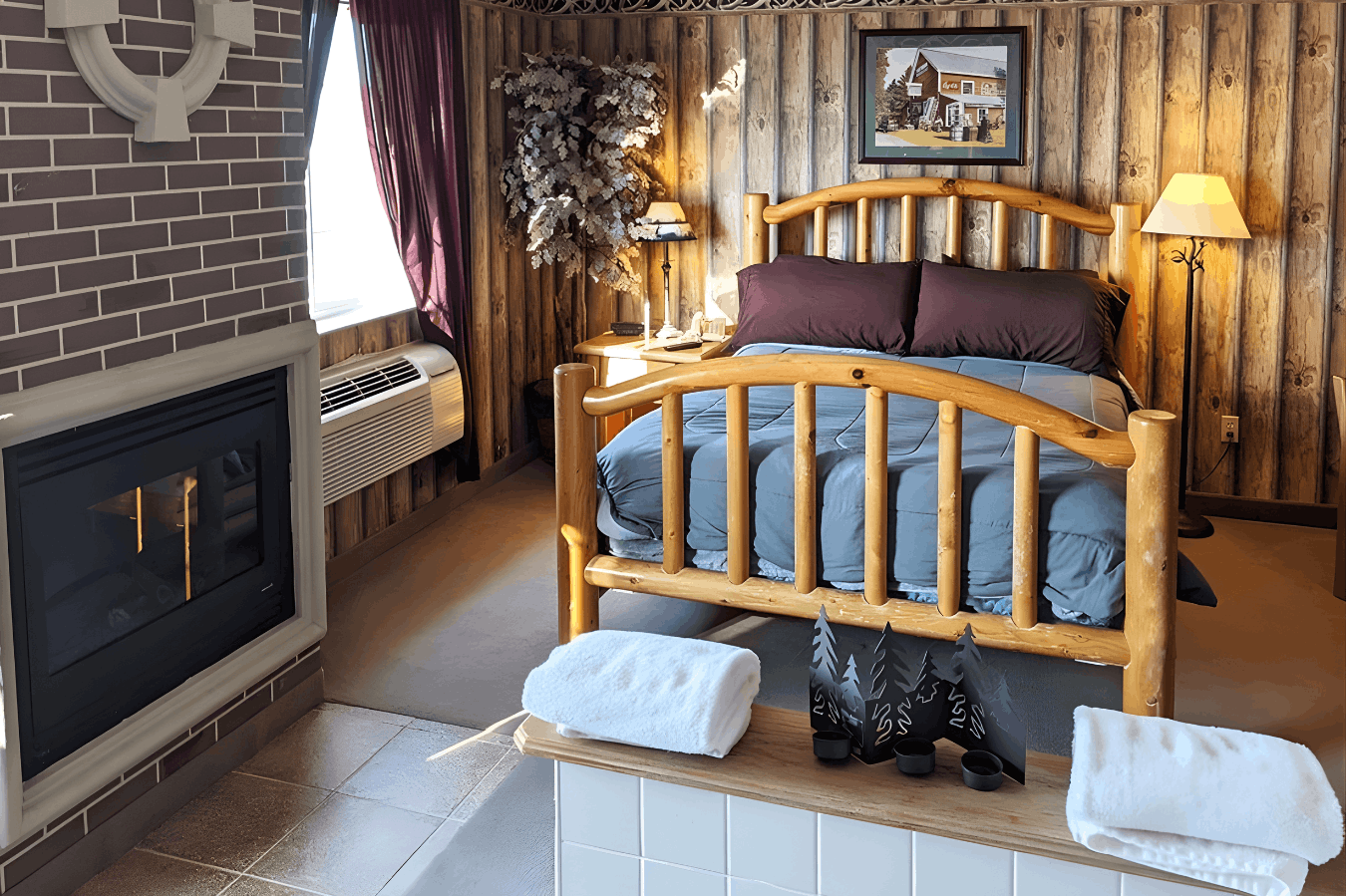 A rustic-themed guest room featuring a log-frame bed, a brick-enclosed fireplace, and wood-paneled walls.